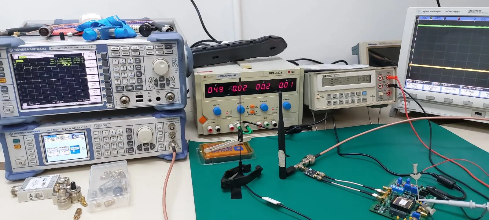 The Altiv Labs bench: Rohde & Schwarz network analyzer and signal generator, regulated power supply, bench multimeter and oscilloscope, with a board under test and an antenna on the mat
